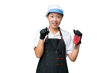 Young caucasian woman wearing an apron and serving fresh cut meat over isolated background surprised and pointing front