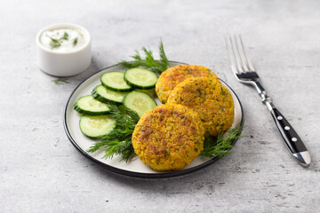 Delicious millet cutlets with carrots and seeds served with cucumber and herbs on a gray textured...