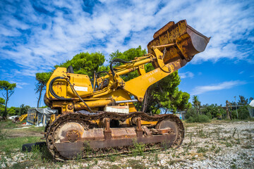 Obraz premium old yellow broken bulldozer. construction machinery with trees in the background