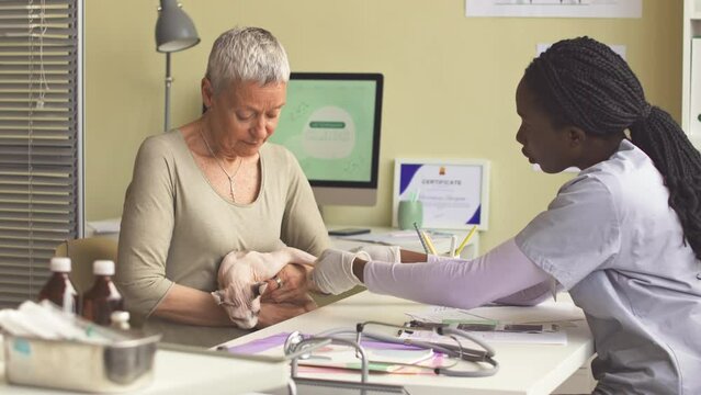 Medium shot of mature Caucasian woman with elf cat visiting veterinary clinic. Young African American female vet examining cats injured leg
