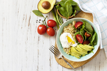 Delicious breakfast or brunch - poached egg, quinoa, avocado and fresh vegetable salad on the kitchen table. Keto diet. View from above. Copy space.