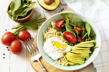 Delicious breakfast or brunch - poached egg, quinoa, avocado and fresh vegetable salad on the kitchen table. Keto diet.