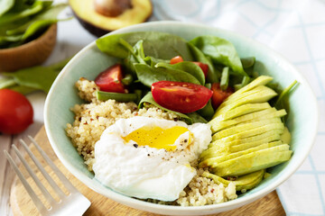 Keto diet. Delicious breakfast or brunch - poached egg, quinoa, avocado and fresh vegetable salad on the kitchen table.