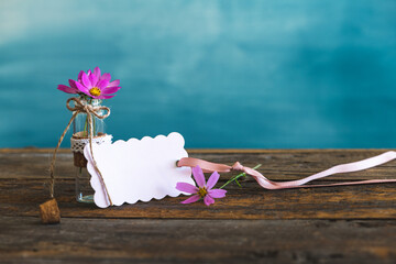 Blank cloud shaped card with cute cosmea flowers in a little glass on a wooden rustic table in front of a turquoise wall - Greeting card 