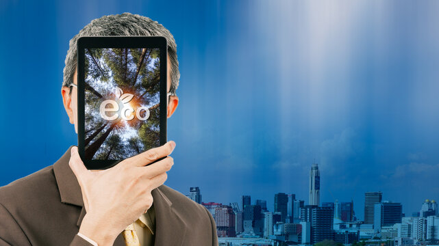 Businessman Showing Picture Of Trees And ECO Icon In His Tablet On City Background. Net Zero Greenhouse Gas Emissions Target. Climate Neutral Long Term Strategy. Net Zero And Carbon Neutral Concept.