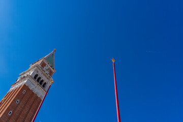 The bell tower in St. Mark's Square in Venice, Italy, goes into the clear sky, where a jet plane flies and a crescent of the moon is visible, on top of the bell tower there are figures of two workers