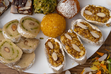 Mix indian sweets like kaju roll dryfruits barfi mango peda served in a plate