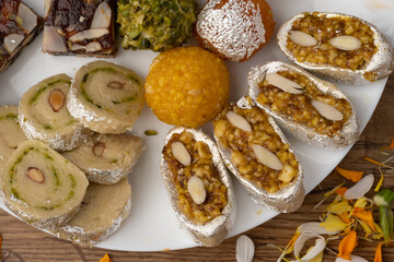 Mix indian sweets like kaju roll dryfruits barfi mango peda served in a plate