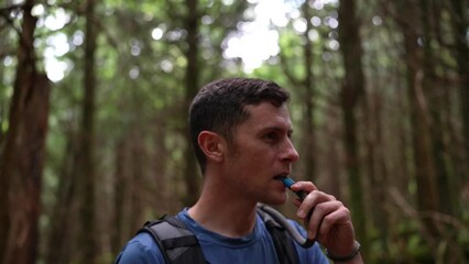 Attractive young man laughs with his hiking companion while taking a drink from a hydration backpack in the forest