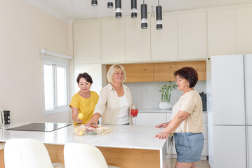 Happy senior women in kitchen cooking together. Mature women in kitchen have fun and prepare salad. A group of friends preparing food together in a kitchen.