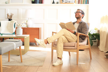 Fototapeta premium Young man is reading a book sitting in a chair at home