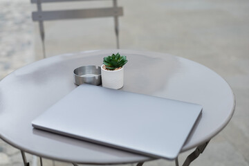 Laptop near plant and ashtray on bistro table outdoors.