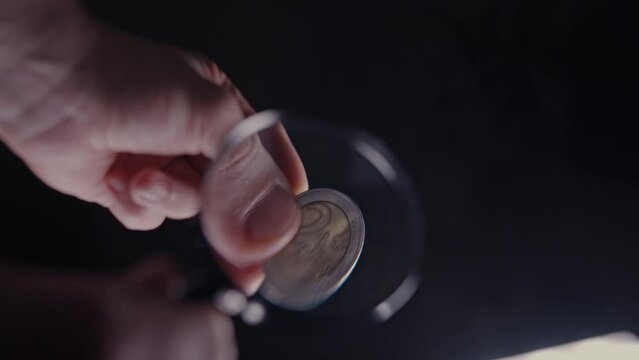 examination of a 2 euro coin under a magnifying glass on a black background close-up, macro shot
