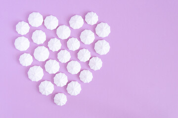 White meringues form a heart shape on a pink background, copy space.