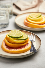 Sliced ​​citrus pyramid on a plate. Orange, grapefruit, lemon and lime showcasing healthy food in a flat lay. Delicious conceptual fruits looks like pancake.Natural beauty, medical concept
