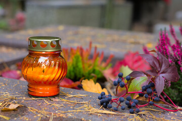 An orange candle on a grave in a cemetery on an autumn day. All Saints Day. Copy space, shallow depth of field.