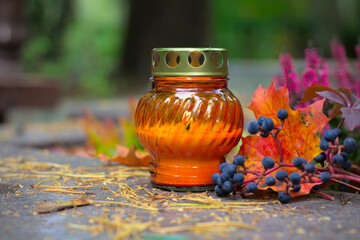 An orange candle on a grave in a cemetery on an autumn day. All Saints Day. Copy space, shallow depth of field.
