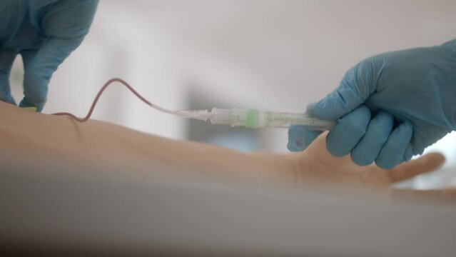 Nurse takes blood through tube into an ampoule from arm on table.
