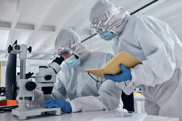 Scientist team, covid research and microscope with team writing notes or results during analysis of...