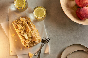 Piece of napoleon cake. Creamy vanilla slice dessert on a parchment paper. Layered baked pie with two glasses of water. Sweet food presentation. Copy space.