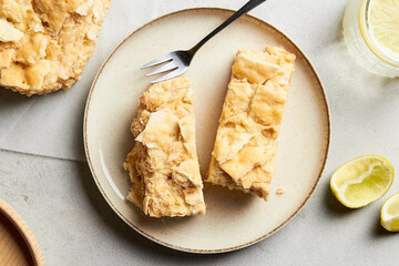 Piece of napoleon cake. Creamy vanilla slice dessert on a plate. Layered baked pie with two glasses of water. Sweet food presentation