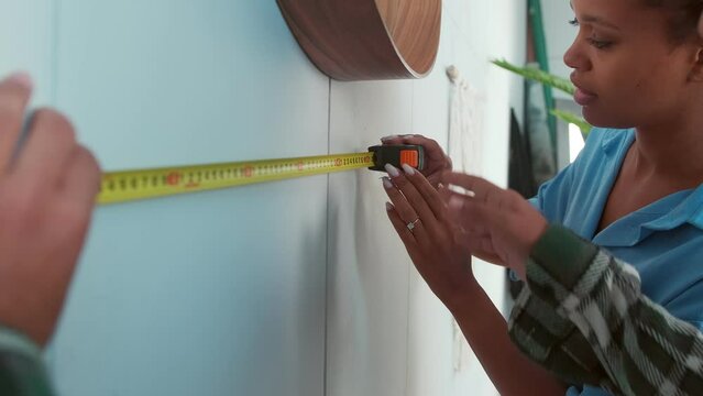 Young attractive ethnic African American woman with boyfriend measure wall with tape-measure wanting to make repairs with their own hands or hang favorite picture in own appartment