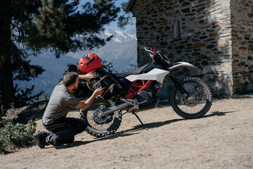 man sitting near his motorcycle during moto trip packs bags on the trunk of a motorcycle in beautiful mountain scenery