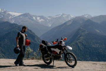 Fototapeta na wymiar man enjoying a mountain view in motorcycle trip holding dry bag on his shoulder going during long journey on enduro motorcycle