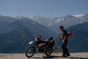 Biker male enjoying a mountain view in motorcycle trip holding dry bag on his shoulder going during long journey on enduro motorcycle