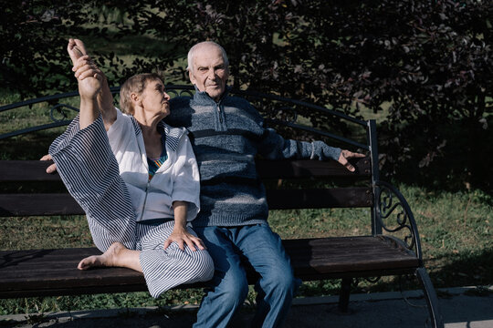 Elderly man and woman couple, husband and wife sitting on park bench hugging and enjoying sunny day and love