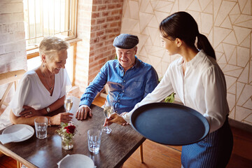 Restaurant waitress, wine glass and service to happy couple for lunch celebration on fine dining date. Hospitality catering, alcohol champagne glasses and drinks menu order to senior customers table