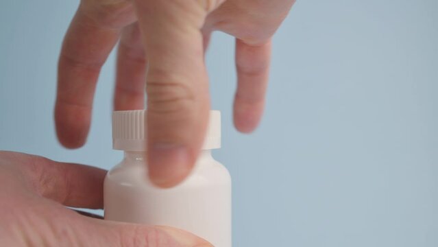 Man pours yellow vitamins pills Omega-3, fish oil into his hand from a white plastic bottle on blue background. Dietary supplement, pills, health care concept, medicine, pharmaceutical products