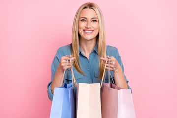 Portrait of satisfied pretty nice woman dressed blue shirt hold shopping bags show you new outfit isolated on pink color background