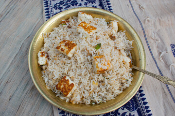 Homemade healthy paneer herb rice or pulav or fried rice in yellow brass plate and spoon with beige and blue background.