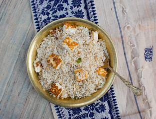 Homemade healthy paneer herb rice or pulav or fried rice in yellow brass plate and spoon with beige and blue background. Top View