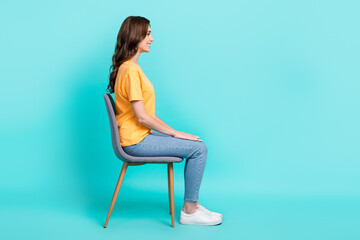 Full length photo of sweet adorable girl dressed yellow t-shirt sitting chair looking empty space isolated teal color background