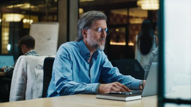Mature businessman working on startup project, business strategy, data analysis in modern office using laptop. Worker of e-commerce marketing company
