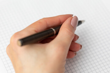 Elegant female hand with a pen over a white sheet of paper. The woman writes with a pen. Premium pen in a female hand. Elegant female hand with perfect manicure. Symbol of business and office work. 