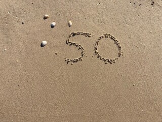 Fototapeta na wymiar On the beach in the sand is carved the number 50