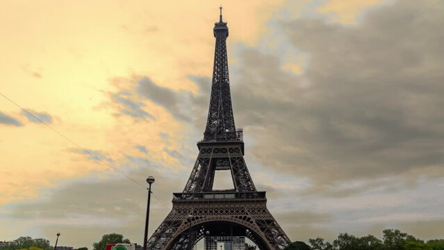 Eiffel Tower in Paris, France: the most famous landmark and tourist attraction in the world - morning hyper-lapse against orange and gray clouds in dramatic stormy sky at sunrise.
