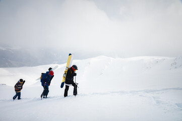 Fototapeta na wymiar group of three backcountry skiers ascending a snowy mountainside on a beautiful foggy snowy day