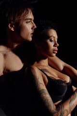 side view of tattooed woman with sexy breast near shirtless man isolated on black.