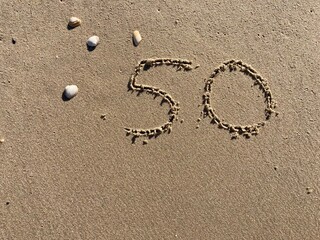 On the beach in the sand is carved the number 50