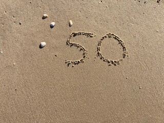 On the beach in the sand is carved the number 50