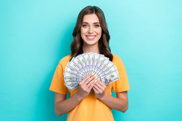 Photo of young pretty attractive gorgeous cute lady wear orange t-shirt hold much cash dollars successful lottery winner isolated on cyan color background