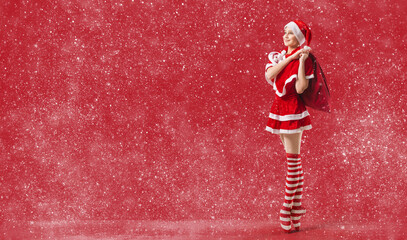 Dancing ballerina girl in pointe shoes with a gift in her hands dressed as Santa Claus on a red background. © Maria Moroz