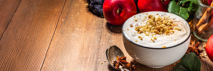 Bowl of homemade apple pie yogurt ready for breakfast, with tart crumble topping. On wooden background with red autumn apples and spices, copy space