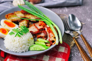 Thai dish '' Khao mu daeng '' or red sauce pork stew with rice and spring onions served in a gray plate on the black table in the restuarant