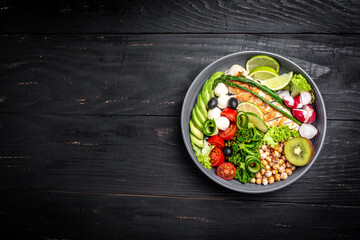 Grilled chicken, avocado, asparagus, chickpeas, broccoli, radish, cucumber, tomatoes, olives, mozzarella buddha bowl on dark background, top view. Delicious balanced food concept