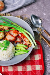 Thai dish '' Khao mu daeng '' or red sauce pork stew with rice and spring onions served in a gray plate on the black table in the restuarant